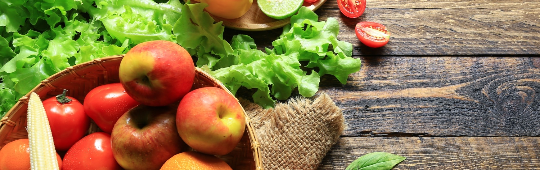 Apples, tomatoes, corn and lettuce on a wood background.